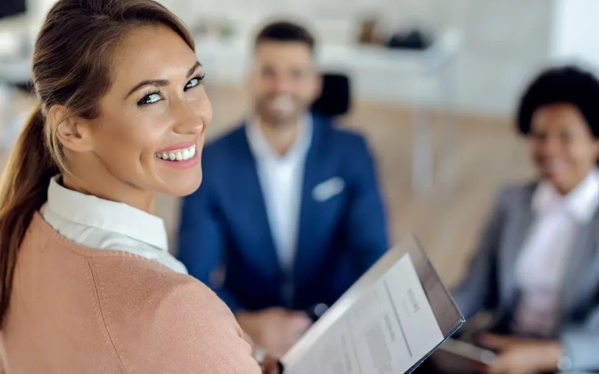 A smiling HR professional holding a resume during an interview, illustrating what human resources do to unlock your team's full potential with C2 Essentials.